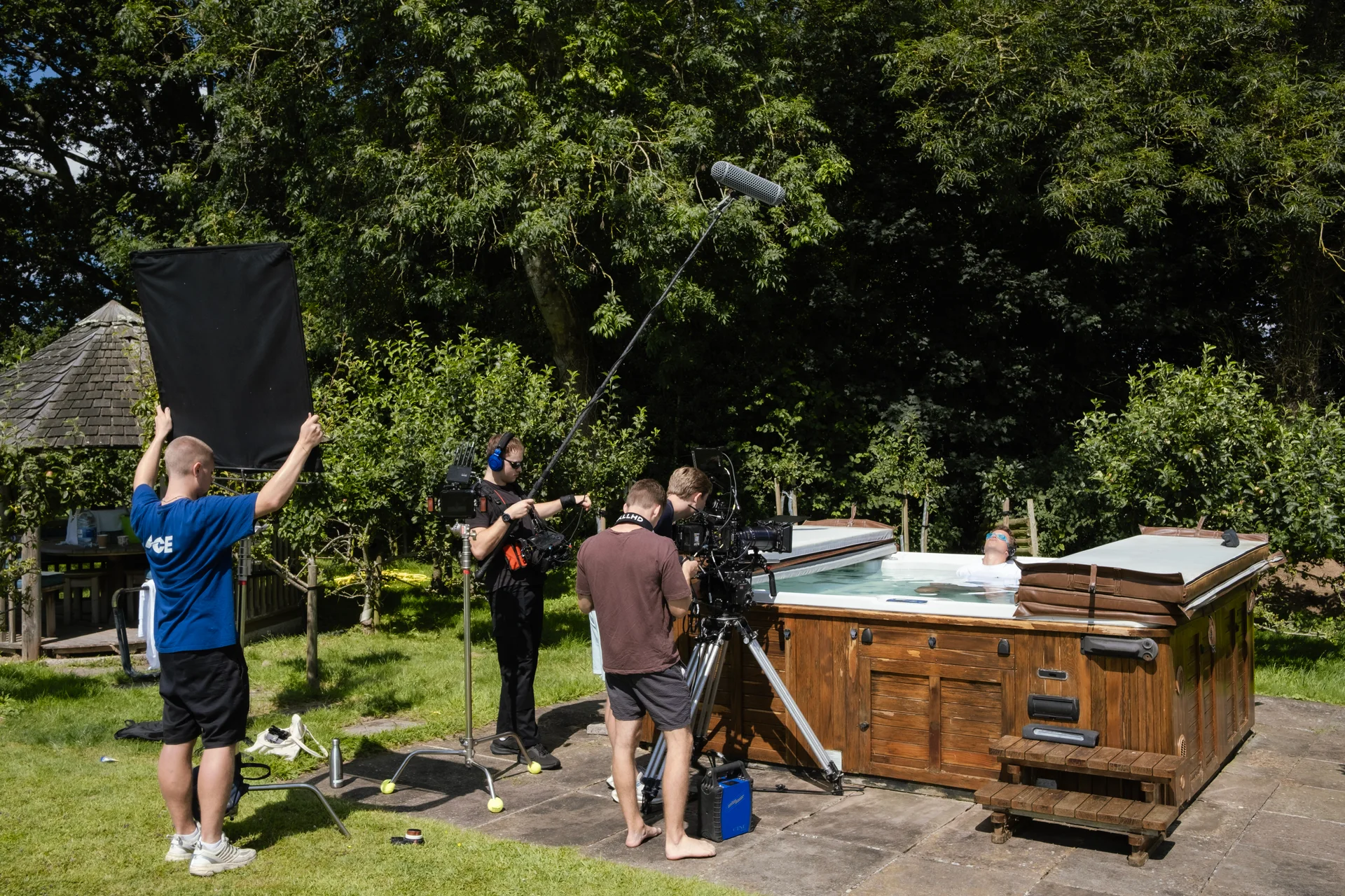 The crew filming Joey Bader in a hot tub, with a lighting flag held overhead