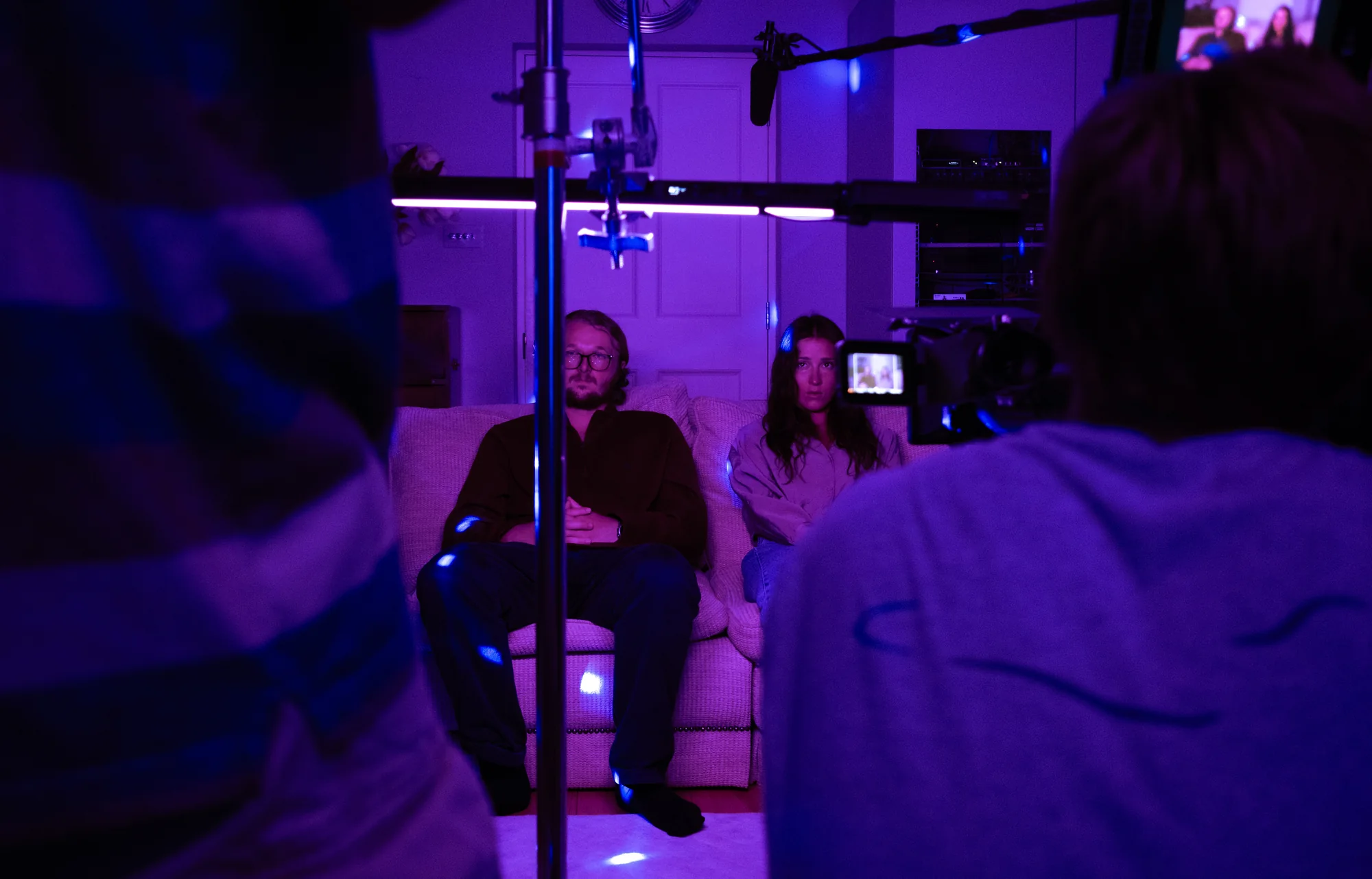 Oliver Woolf and Kaylee McGregor on the sofa, surrounded by cameras and purple lighting